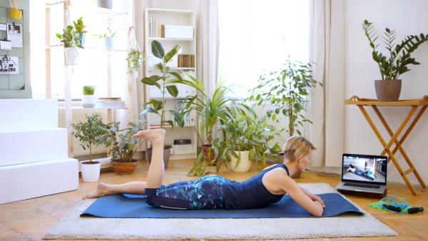 Side view of young woman doing exercise indoors at home, following sport vlogger.