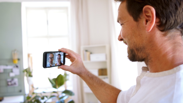 Mature man having video call on smartphone in home office, discussing issues.