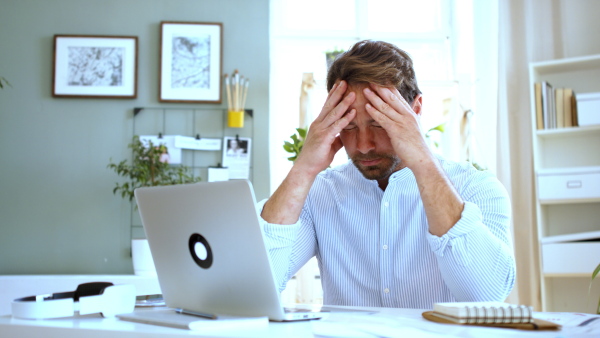 Frustrated and disappointed mature businessman with laptop indoors in home office, working.