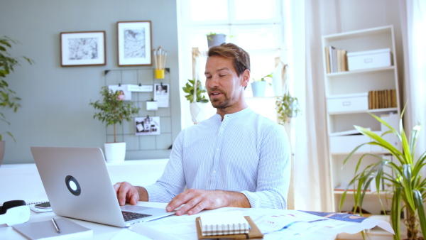 Mature businessman having video call on laptop at home, talking.