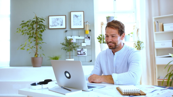 Mature businessman having video call on laptop at home, laughing.