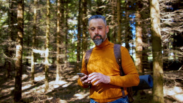 Front view of nature man with backpack and smartphone outdoors in forest in nature, looking at camera.