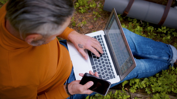 Top view of man with laptop and smartphone in forest in nature, outdoor office concept. Slow motion.