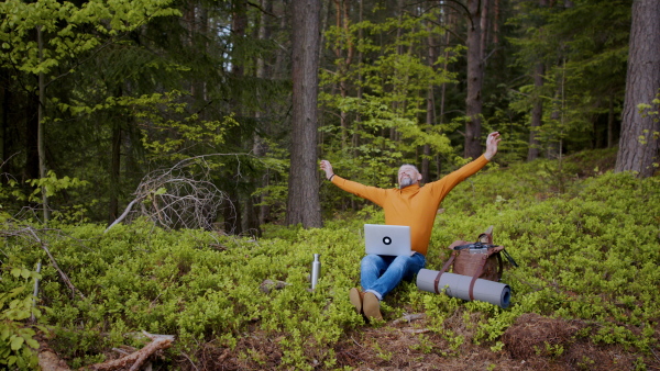 Tired mature man with laptop stretching in forest in nature, outdoor office concept.