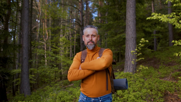 Happy mature man with backpack outdoors in forest in nature, walking. Slow motion.