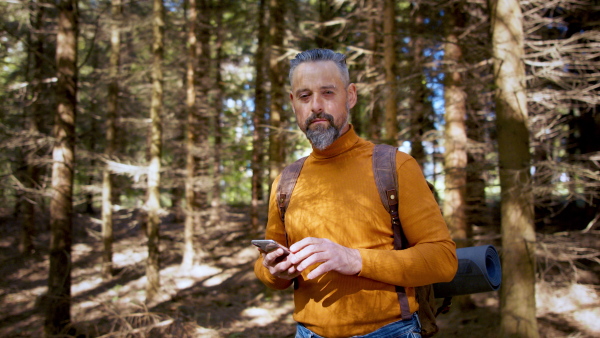 Front view of nature man with backpack and smartphone outdoors in forest in nature, looking at camera.