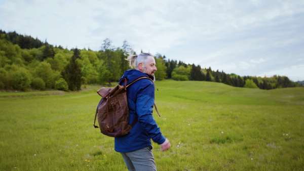 Front view of mature man with backpack running outdoors on grassland in nature. Slow motion.