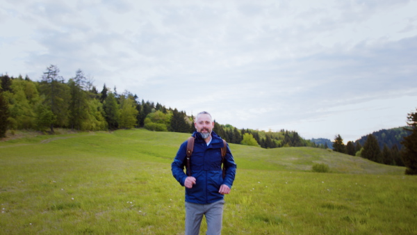 Front view of mature man with backpack running outdoors on grassland in nature.