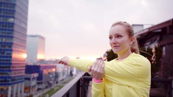 Young woman in yellow tracksuit doing stretching after run.