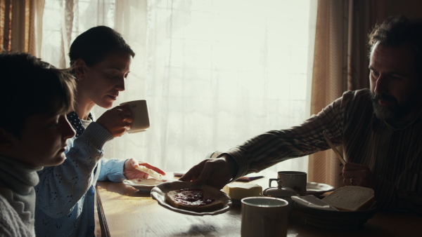 A side view of unhappy poor family having a breakfast indoors at home, poverty concept.