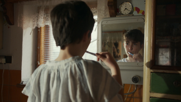 A rear view of poor sad small girl brushing her teeth at home, poverty concept.