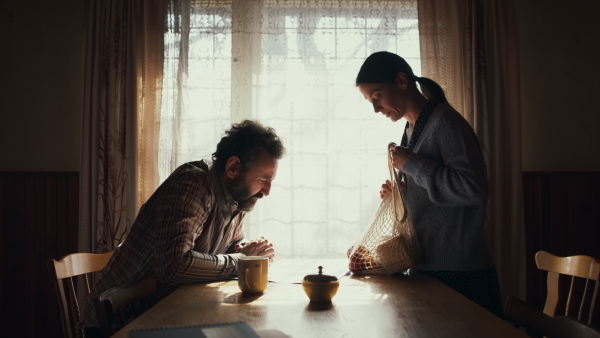 Side view of poor mature couple sitting indoors at home, poverty concept.