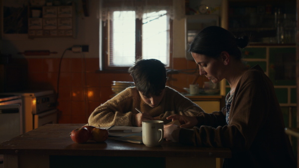 Portrait of sad poor mother helping small daughter with school indoors at home, poverty concept.