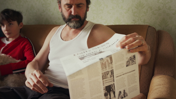 Poor family sitting on sofa in living room, father reading a newspapers. Poverty concept.