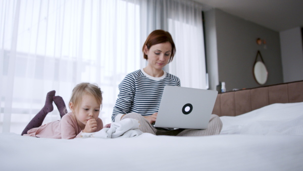 Mother working from home next to her daughter on bed. Homeoffice concept.