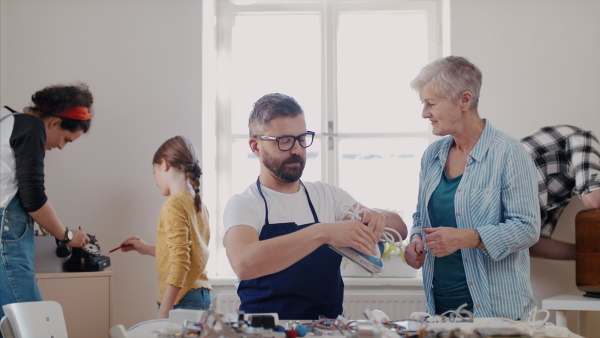 A group of old and young people at repair cafe repairing household electrical devices.