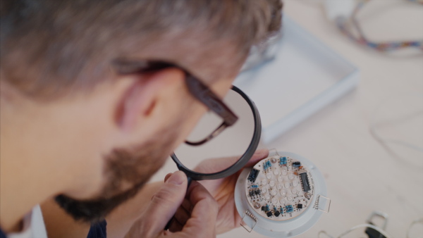 Close-up of man with magnifying glass at repair cafe repairing household electrical devices, midsection.