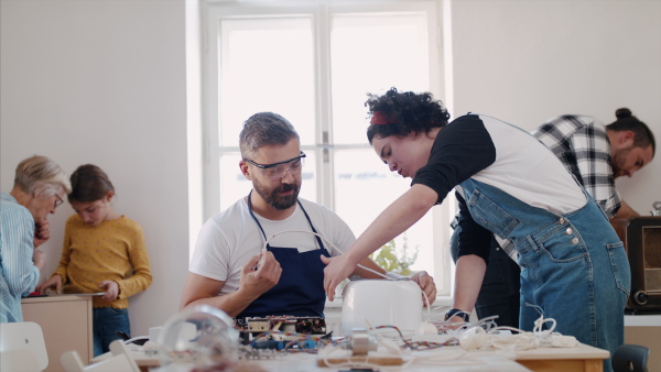 A group of old and young people at repair cafe repairing household electrical devices.