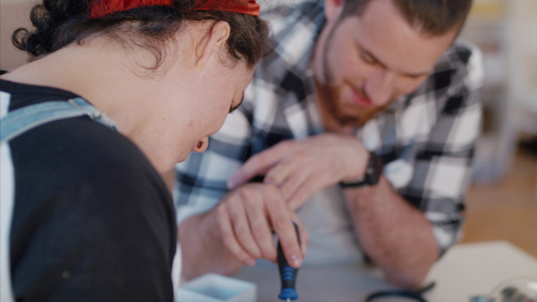 A young couple at repair cafe repairing household electrical devices, talking.