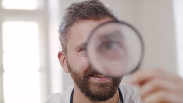 Front view of mature man with magnifying glass at repair cafe looking at camera.