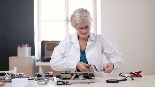 Front view of senior woman at repair cafe repairing household electrical devices.