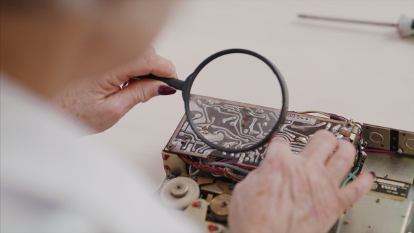 Unrecognizable senior woman at repair cafe repairing household electrical devices.