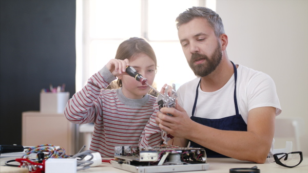 Small girl with mature man at repair cafe repairing household electrical devices.