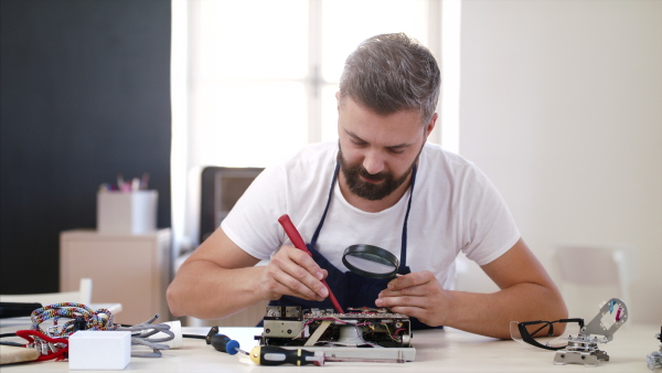 A mature man with magnifying glass at repair cafe repairing household electrical devices.