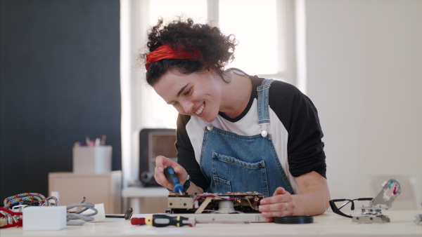 Front view of young woman at repair cafe repairing household electrical devices.