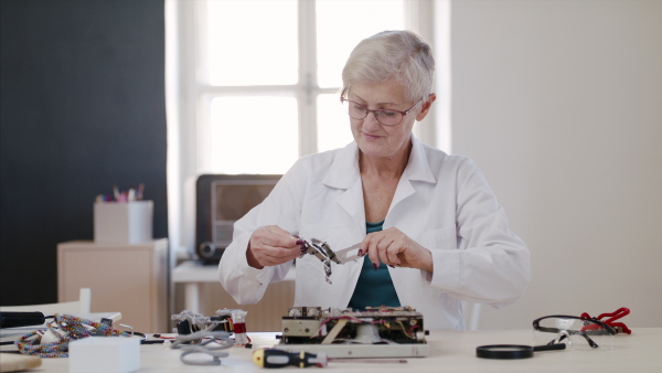 Front view of senior woman at repair cafe repairing household electrical devices.