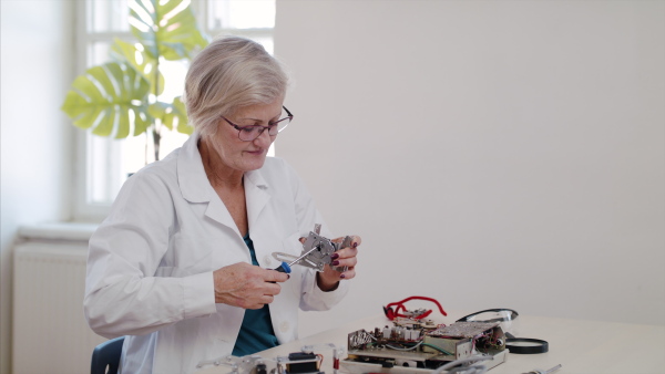 Front view of senior woman at repair cafe repairing household electrical devices.