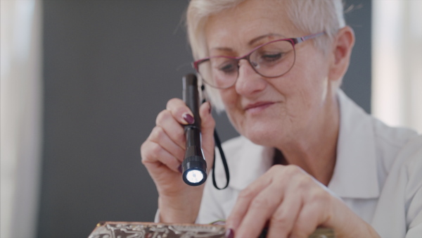 A senior woman with torch at repair cafe repairing household electrical devices.