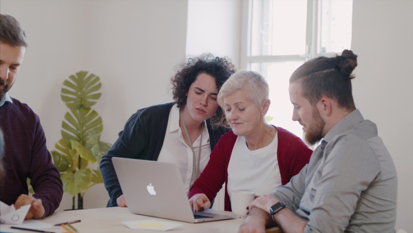 A group of young and old people with laptop at community centre, talking.