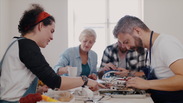 A group of old and young people at repair cafe repairing household electrical devices.