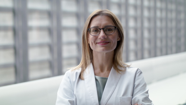 A portrait of female doctor standing on corridor, looking at camera.