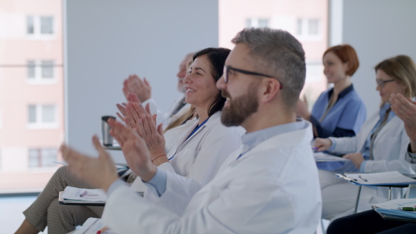 A group of doctors listening to presentation on medical conference, clapping.