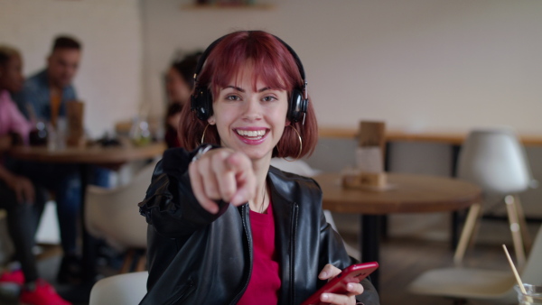 Young woman sitting in cafe, using headphones and smartphone, listening to music. Slow motion.