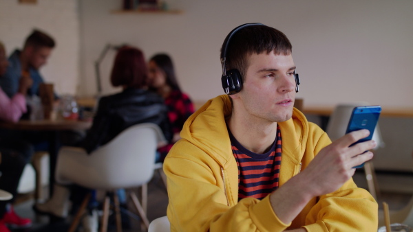 Portrait of young man with headphones and smartphone sitting in cafe, listening to music.