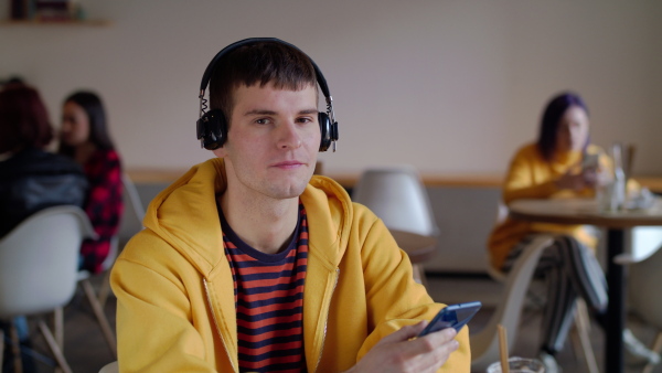 Portrait of young man with headphones and smartphone sitting in cafe, listening to music.