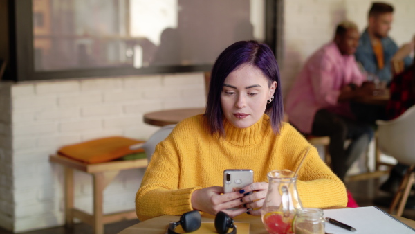 Front view portrait of happy young woman sitting in cafe, using smartphone.