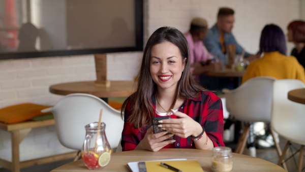 Front view portrait of happy young woman sitting in cafe, using smartphone. Slow motion.