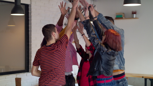 A group of cheerful young friends standing in cafe, giving high five. Slow motion.