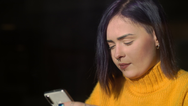 Close-up portrait of young woman sitting in cafe, using smartphone.