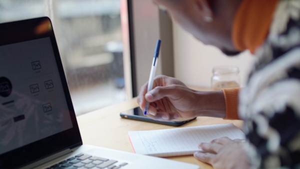 A close-up of young man working and writing in cafe, using laptop.