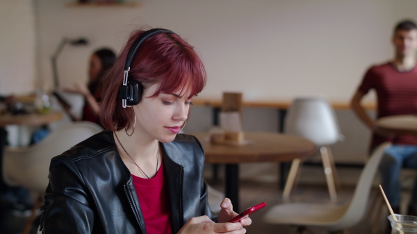 Young woman sitting in cafe, using headphones and smartphone, listening to music.