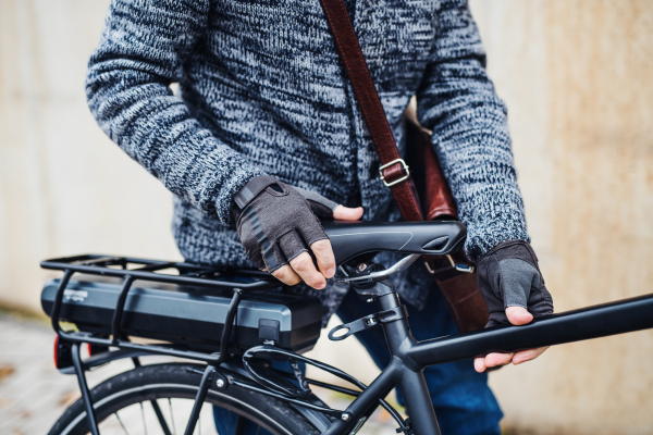 A midsection of an unrecognizable cyclist with electrobike standing outdoors in town.