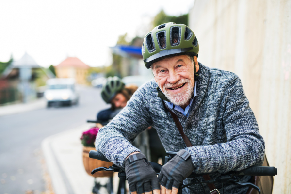 Active senior couple with helmets and electrobikes standing outdoors on a road in town.