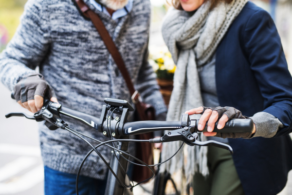 A midsection of active senior couple with electrobike standing outdoors on a road in town.