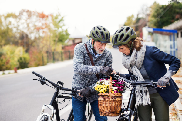 Active senior couple with helmets and electrobikes standing outdoors on a road in town.