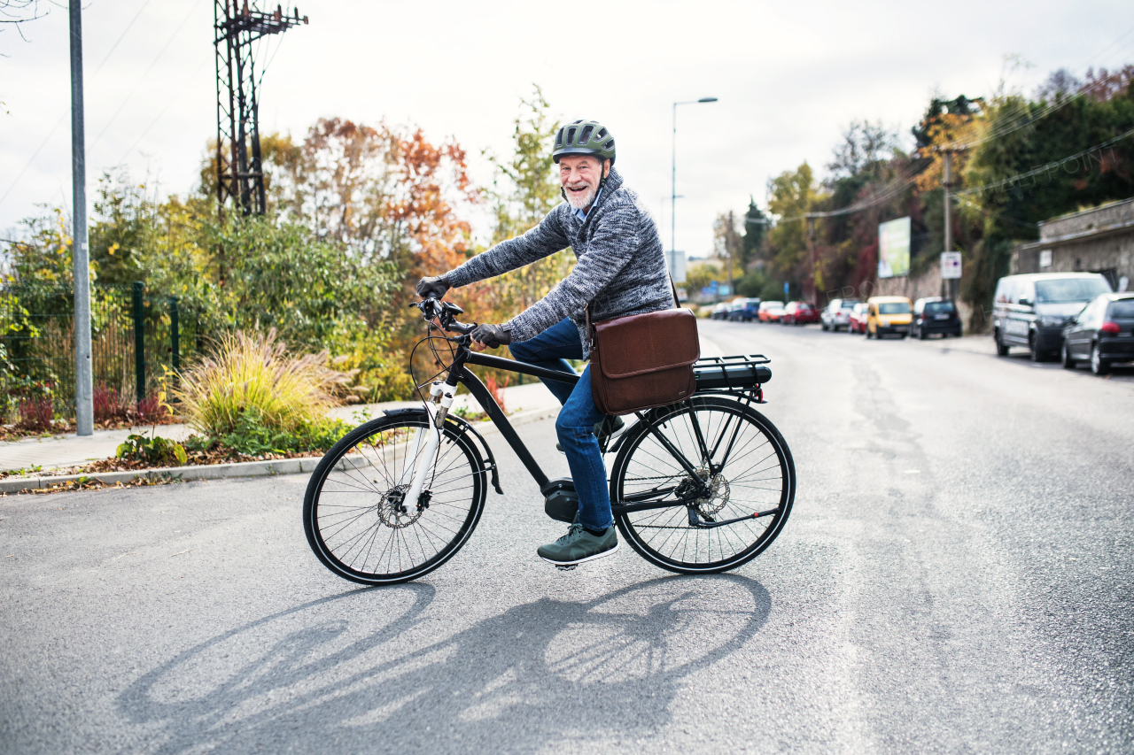 An active senior man with helmet and electrobike cycling outdoors in autumn in town.